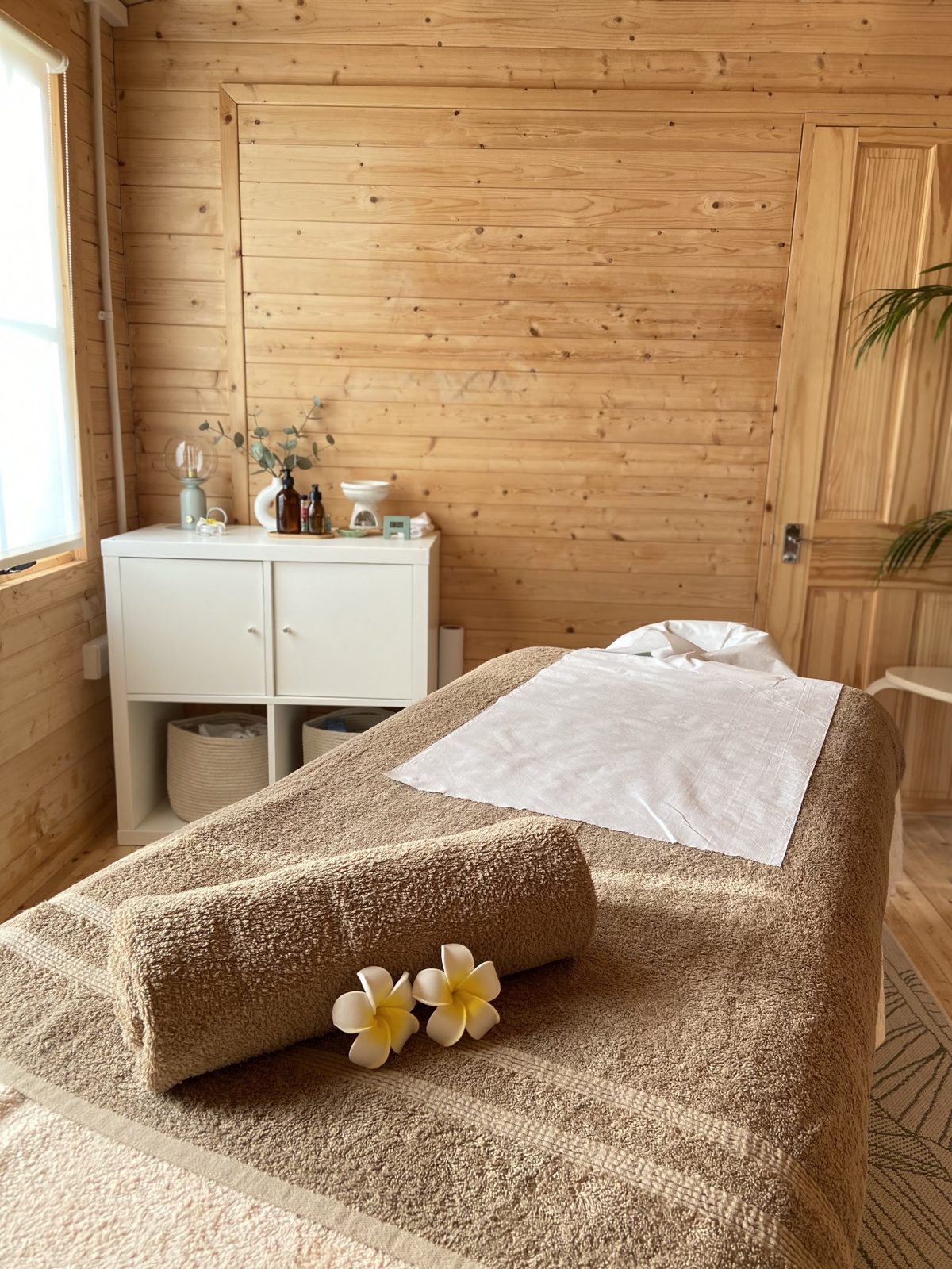 Our massage couch made up with a rolled towel and frangipani flowers in the timber treatment room