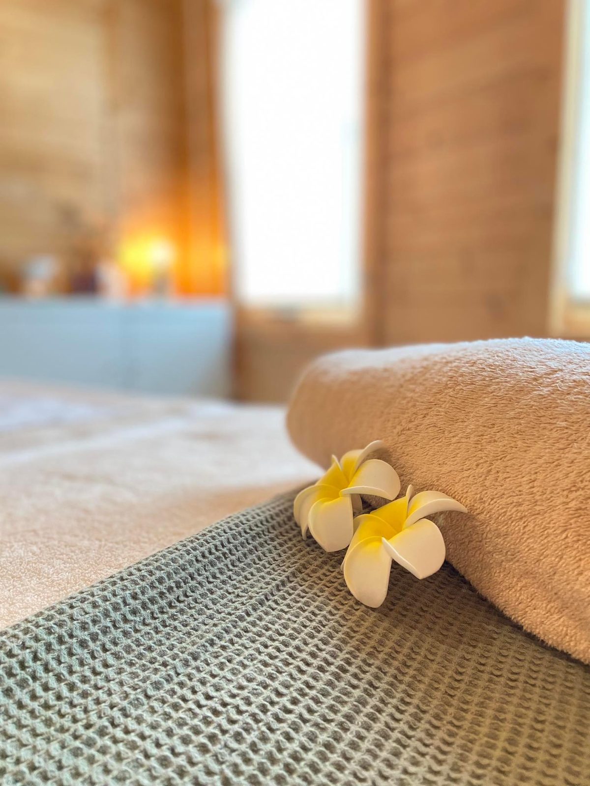A rolled towel with frangipani flowers on the massage couch