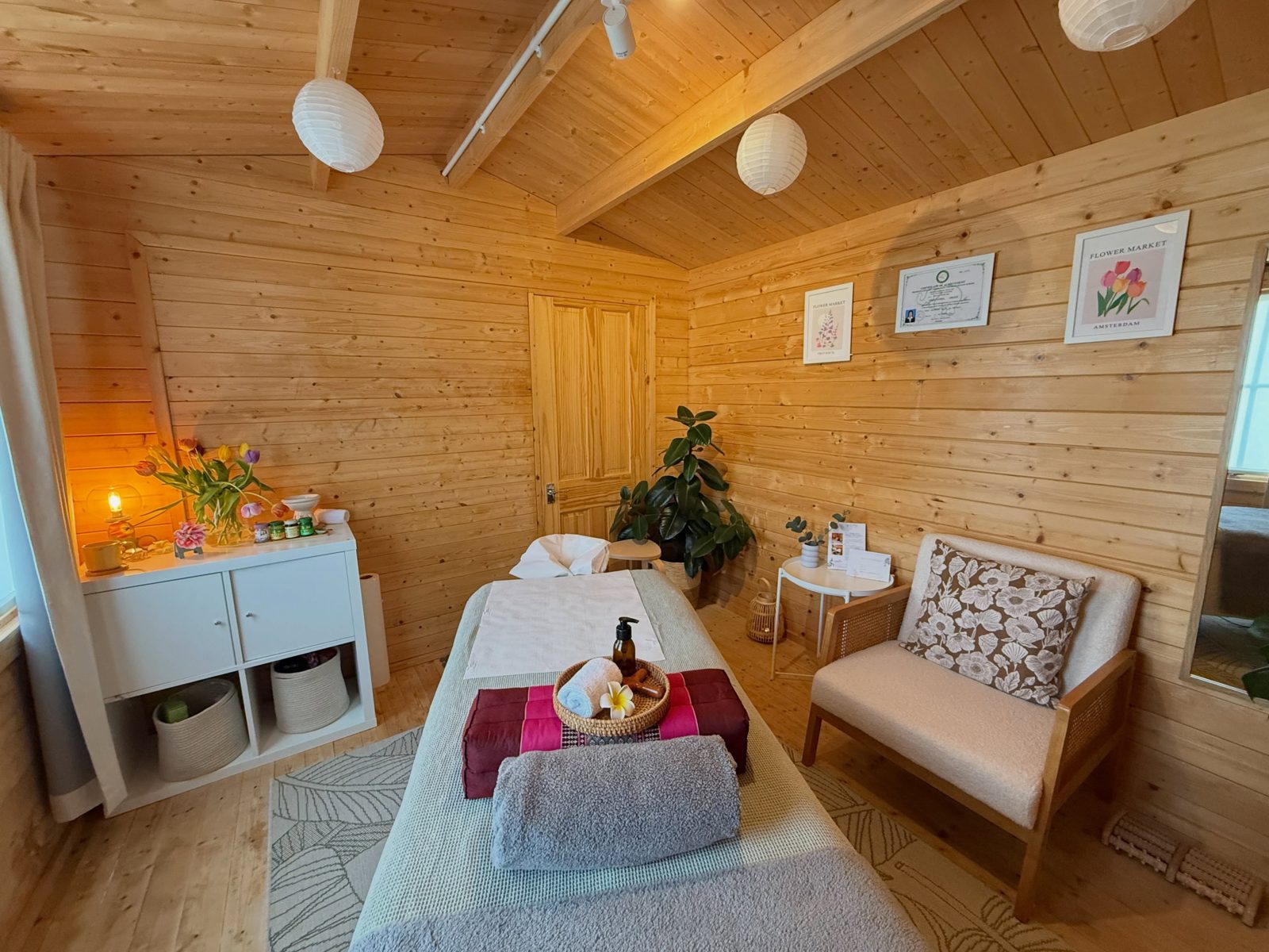 The timber-clad treatment room with the massage couch, lanterns, an armchair and flowers
